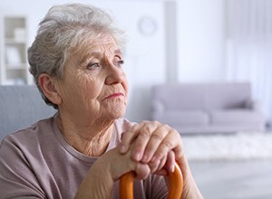 Sad senior woman resting her hands on her cane